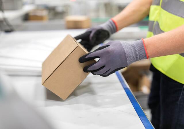 倉庫のベルトコンベアの上で作業員に確認される箱
